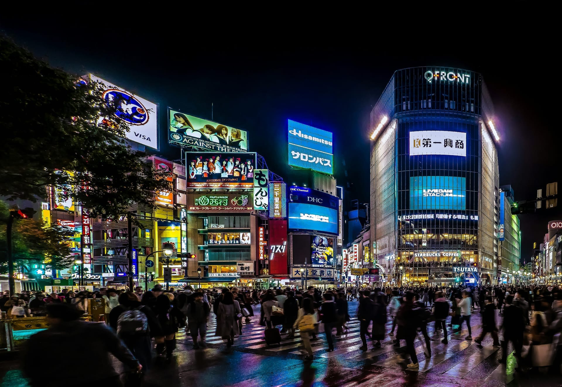 Shibuya Crossing at night with glowing neon signs and the QFRONT building illuminated against a dark sky